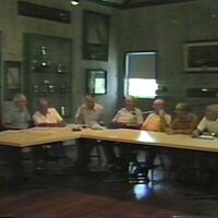 John Kochiss and various baymen sitting around a table at the Long Island Maritime Museum during a recording session of the baymen’s oral history group, June 19, 1985 (Image taken from a video tape).