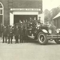 Group of firemen in uniform posing with fire truck out front of firehall at 21 High St.