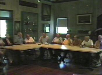 John Kochiss and various baymen sitting around a table at the Long Island Maritime Museum during a recording session of the baymen’s oral history group, June 19, 1985 (Image taken from a video tape).